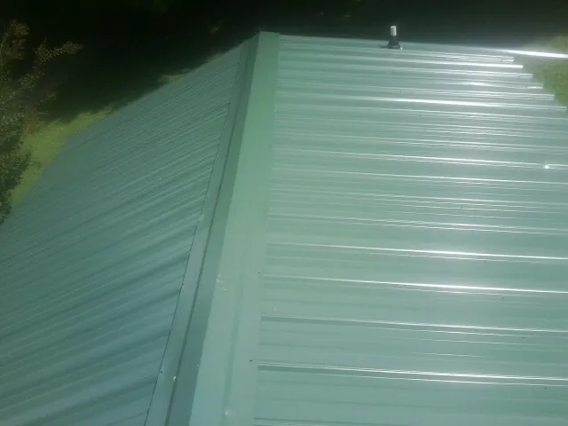 New green metal panels meeting at the ridge of a roof — Flat Roof Repair work by our crew in Dixie
